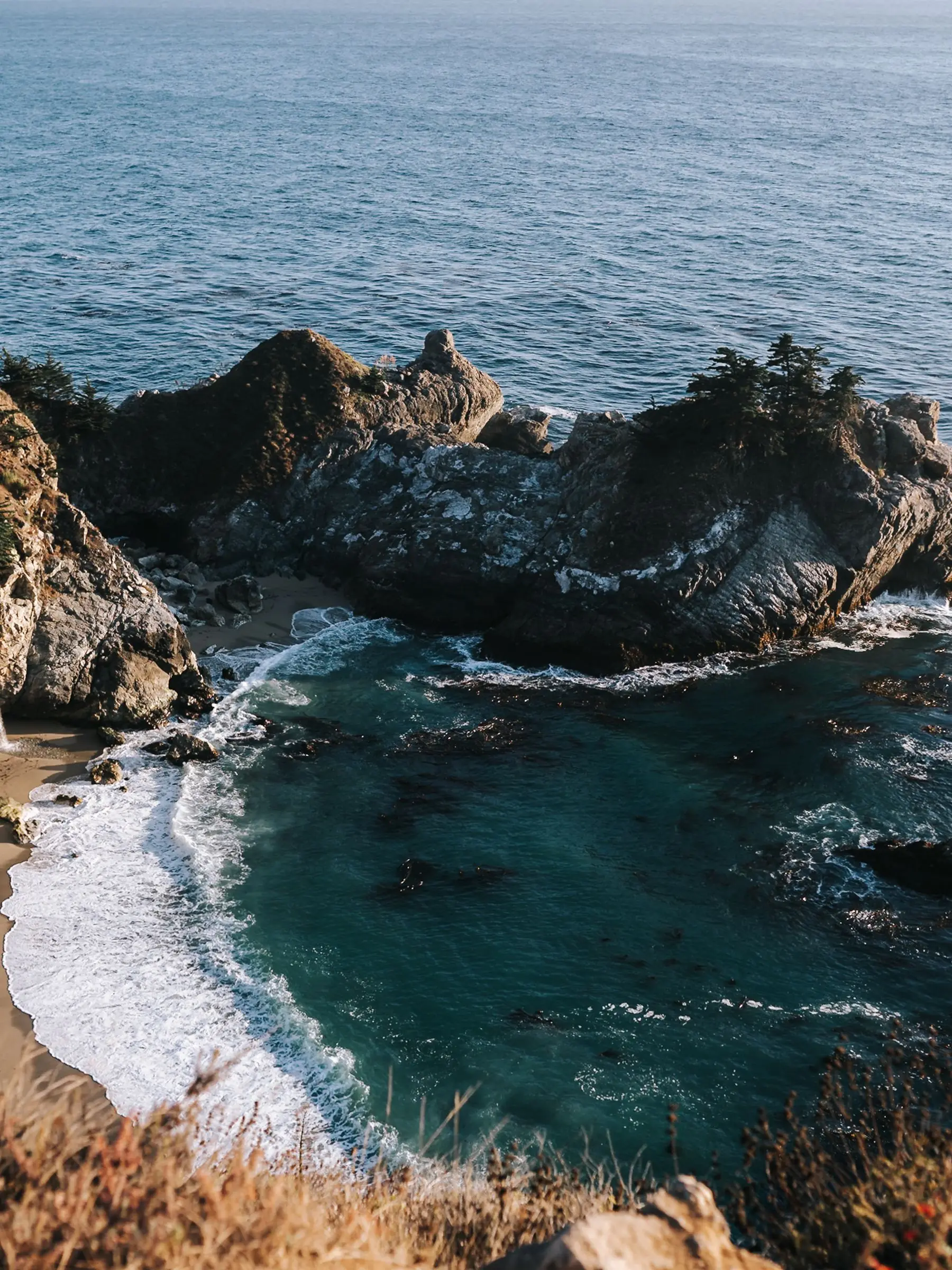 An aerial view of a sandy Big Sur cove enclosed by cliffs