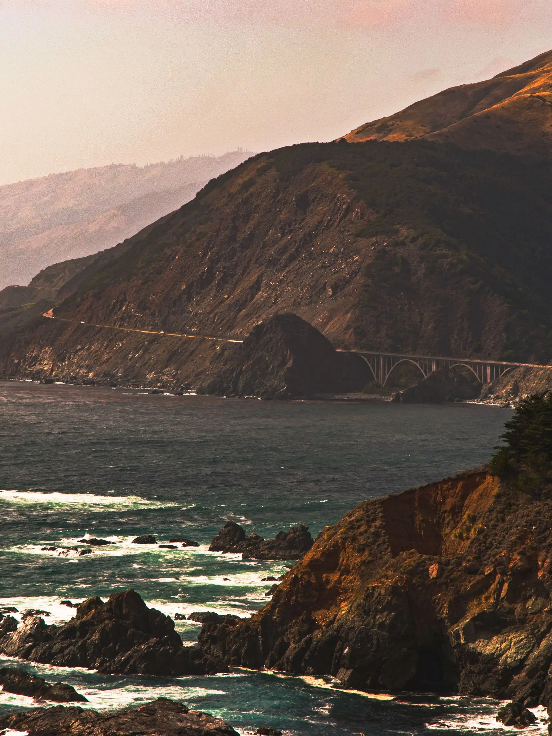 Waves breaking against a rocky headland below coastal hills