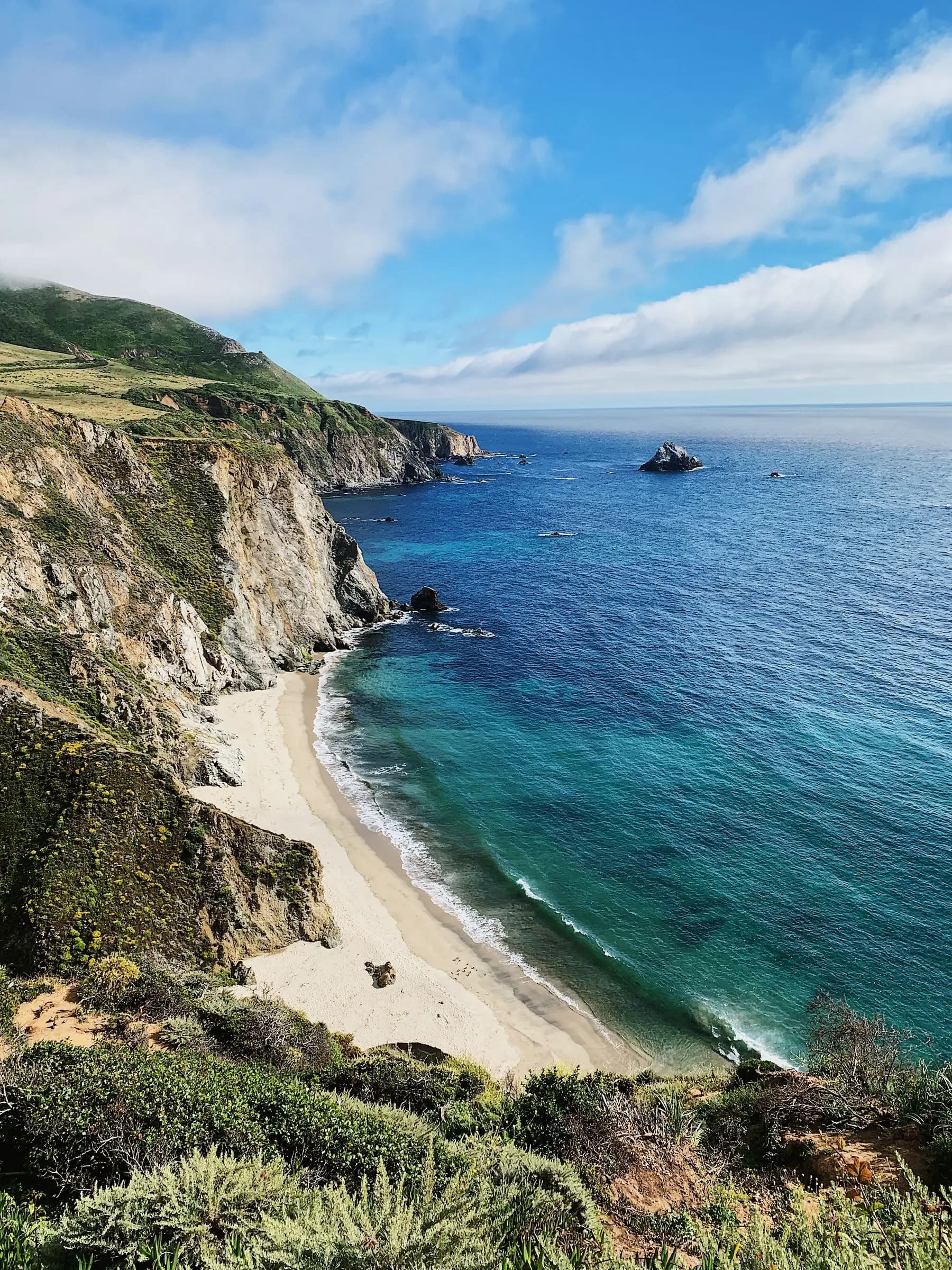 Green coastal mountains above a turquoise shoreline under a clear sky